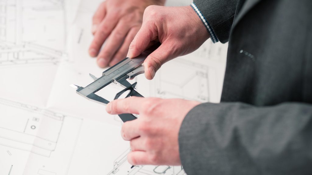 Hände eines Konstrukteurs über Plänen, Skizzen mit Messschieber